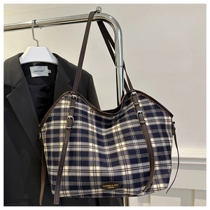 Detail of blue plaid tote bag with adjustable leather strap and metal logo plaque
