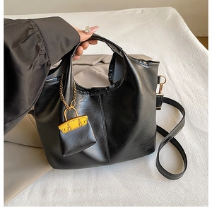 Détail du sac seau en cuir noir texturé avec un mini charm jaune et des boucles dorées