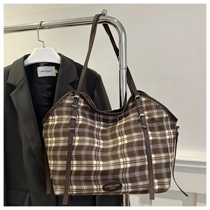 Detail of checkered canvas tote bag with brown leather straps and brand logo patch