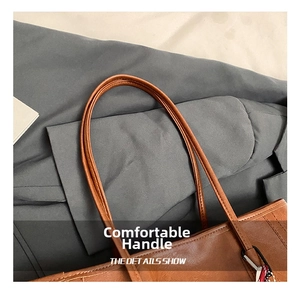 Detail of tan pebble leather tote showing slim handles and reinforced stitching