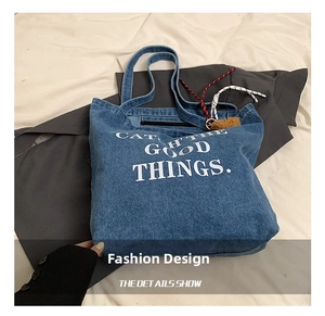Close-up of blue denim tote bag featuring white printed letters and secure zipper closure