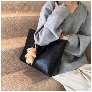 Detail of a black faux leather tote bag with a beige plush bear and printed silk scarf