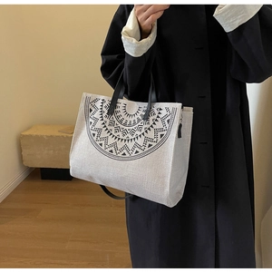 Side view of white canvas tote bag with black geometric print and leather straps