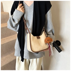 Detail of minimalist cream shoulder bag with brown trim and plush bear charm accent