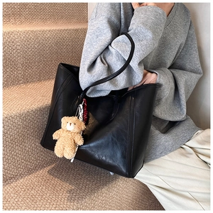 Close-up of black leather tote bag with vertical stitching and brown bear charm