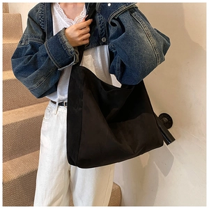 Detail of a black faux suede tote bag showing the textured material and wide shoulder strap