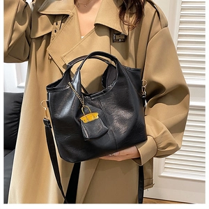 Détail du sac seau en cuir noir souple avec un petit pendentif de sac jaune élégant