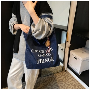 Detail of blue denim tote bag with white lettering and a brown plush bear keychain