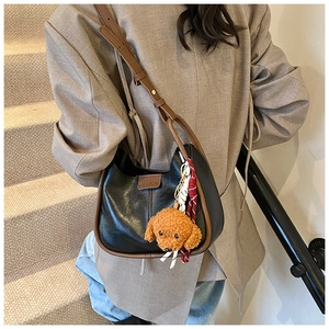 Detail of color-block shoulder bag with plush dog charm and adjustable leather strap
