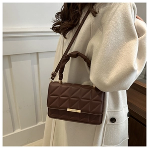 Detail of brown quilted shoulder bag with gold rectangular lock on a model in wool coat
