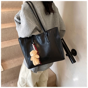 Detail of a black minimalist faux leather tote bag with a cute plush bear charm accessory