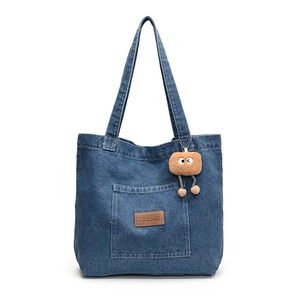 Sac fourre-tout en jean bleu délavé avec poche extérieure et breloque en peluche sur fond blanc