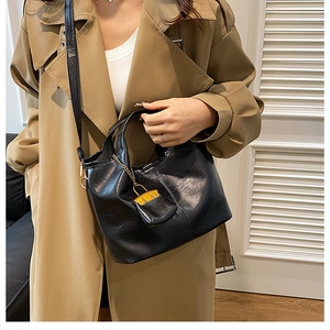 Détail du sac seau noir en similicuir avec mini pendentif porté sur un trench-coat beige