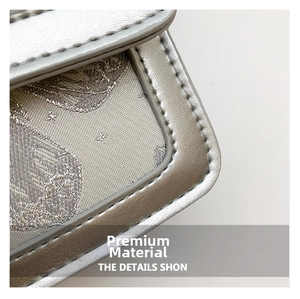 Macro detail of silver fabric with leaf patterns and premium leather stitching on the bag