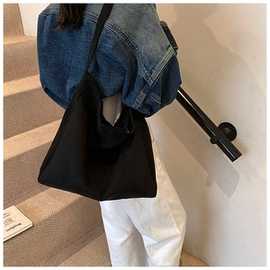 Minimalist black tote bag with wide strap worn by a model on stairs for daily style