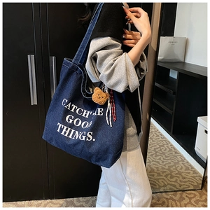Detail of blue denim tote bag with Catch The Good Things slogan and brown bear charm