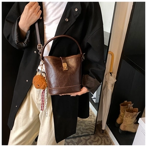 Detail of vintage brown bucket bag with textured leather, gold clasp, and plush bear charm