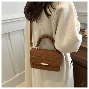 Detail of brown quilted shoulder bag with ruched handle and metal clasp on white coat