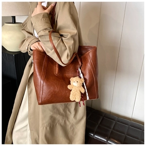 Close-up of vintage brown leather tote bag with a cute plush teddy bear charm detail