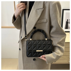 Detail of black quilted handbag featuring a ruched handle and elegant gold-tone hardware