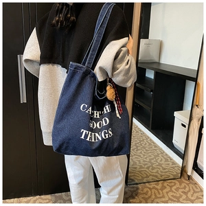 Detail of dark blue denim tote bag with white text print and plush bear keychain