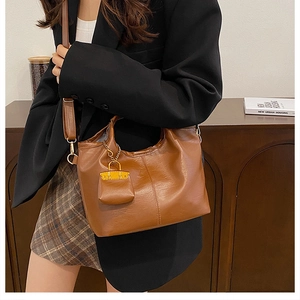 Detail of brown faux leather bucket bag with pebble texture and mini charm pouch