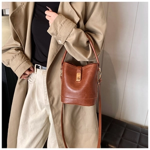 Close-up of brown vintage bucket bag with gold clasp shown on a trench coat model