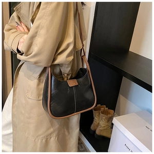 Detail of minimalist leather shoulder bag featuring black body and brown trim accents