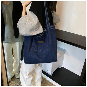 Detail of blue denim tote bag featuring a functional outer pocket and brown faux leather patch