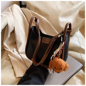 Detail of color-block tote bag with a brown teddy bear charm on a cream leather sofa