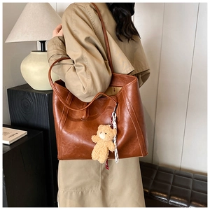 Detail of a deep brown faux leather tote bag featuring a cute plush bear charm accessory