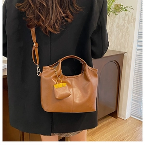 Gros plan d'un sac seau marron avec une petite pochette porté avec un blazer noir chic