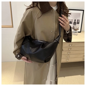 Dettaglio della borsa a nuvola plissettata nera in pelle indossata con un trench coat