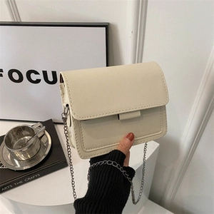 Detail der cremeweißen Ledertasche mit dunkelgrauer Metallkette in modernem Ambiente
