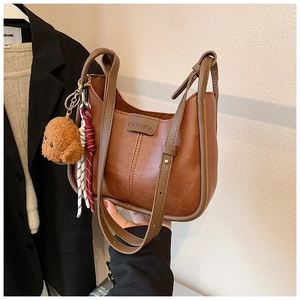 Brown vintage faux leather handbag detail featuring a cute plush bear charm and fashion text