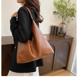 Side view of large brown faux leather hobo tote bag worn by model in a minimalist home setting