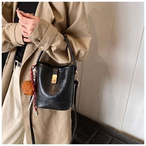 Detailed view of a black bucket bag with gold twist lock and cute plush bear charm