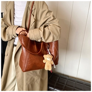 Brown leather tote bag with plush bear charm and clear lychee grain texture details