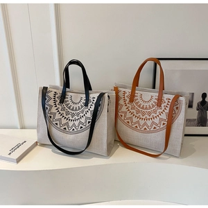 Close-up of canvas tote bag with geometric tribal totem and leather handles on white display