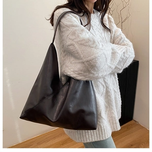 Women's dark coffee brown faux leather tote bag worn over the shoulder with a sweater