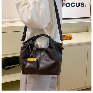 Detail of black leather bucket bag with thick handle and yellow mini charm accessory