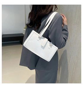 Detail of a white leather rectangle shoulder bag with gold hardware on a model