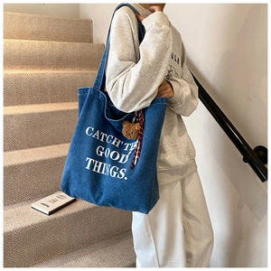Detail of blue denim tote bag featuring white slogan and cute brown bear pendant