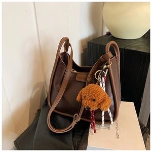 Detail of dark brown faux leather handbag featuring dual handles and a cute teddy bear charm