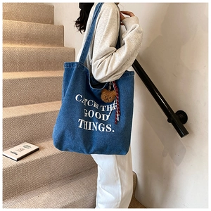 Detail view of blue denim tote bag featuring white CATCH THE GOOD THINGS print and bear charm
