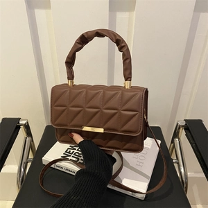 Brown quilted crossbody bag with cloud handle and gold clasp on a stack of books