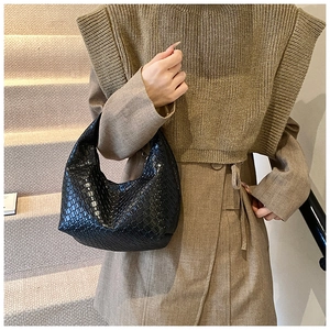 Detail of a black woven hobo bag held by a model on a staircase for a vintage style