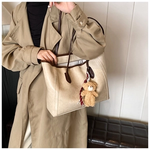 Detail of beige tote bag with brown trim and cute plush bear charm on a trench coat