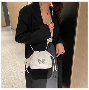 Close-up of white drawstring bucket bag with silver butterfly and plush pompom charm