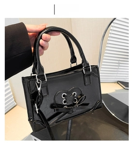 Close-up of black patent leather handbag featuring heart lace-up detail and slim shoulder strap